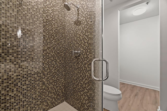 bathroom featuring a shower stall, toilet, wood finished floors, and baseboards