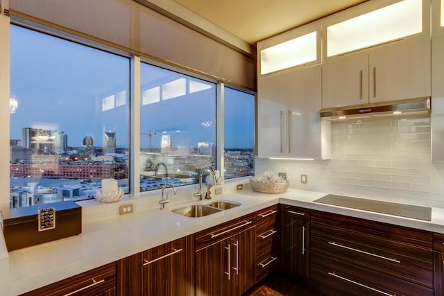 kitchen with a sink, light countertops, backsplash, a view of city, and black stovetop