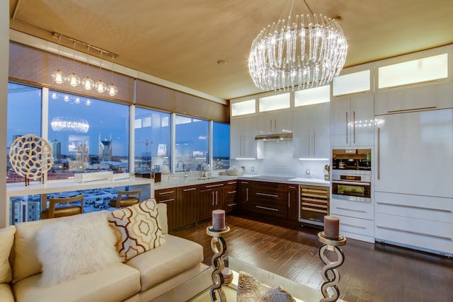 kitchen with dark wood-type flooring, beverage cooler, built in fridge, an inviting chandelier, and double oven