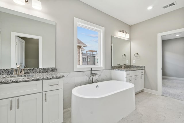 full bathroom featuring a freestanding tub, two vanities, a sink, and visible vents