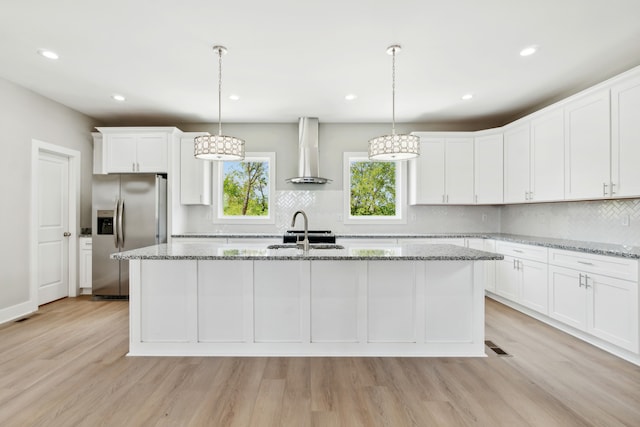 kitchen with wall chimney exhaust hood, light wood-type flooring, stainless steel fridge, and light stone counters