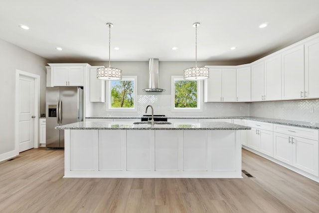 kitchen with white cabinetry, light wood-style floors, stainless steel fridge with ice dispenser, wall chimney exhaust hood, and a center island with sink