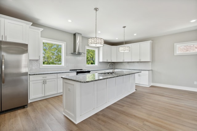 kitchen with light hardwood / wood-style flooring, wall chimney exhaust hood, tasteful backsplash, stainless steel appliances, and a center island with sink