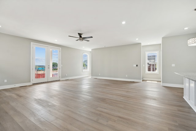 unfurnished living room with light wood-type flooring, french doors, ceiling fan, and a healthy amount of sunlight