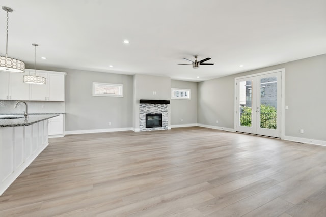 unfurnished living room featuring a wealth of natural light, light wood-type flooring, a fireplace, and ceiling fan