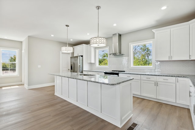 kitchen with light hardwood / wood-style flooring, tasteful backsplash, wall chimney exhaust hood, and stainless steel appliances