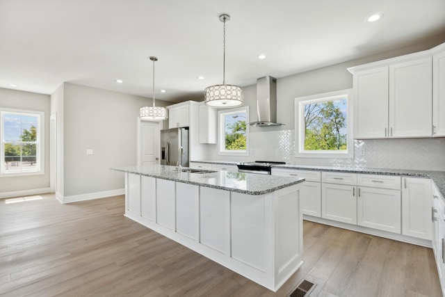 kitchen featuring a center island with sink, light wood finished floors, stainless steel appliances, visible vents, and wall chimney range hood