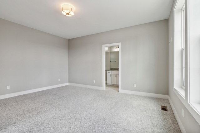 unfurnished bedroom with ensuite bathroom and light carpet