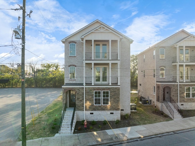 view of front of home with french doors, brick siding, crawl space, a balcony, and stone siding