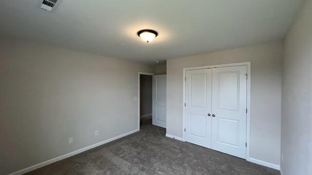 unfurnished bedroom with a closet, dark carpet, visible vents, and baseboards