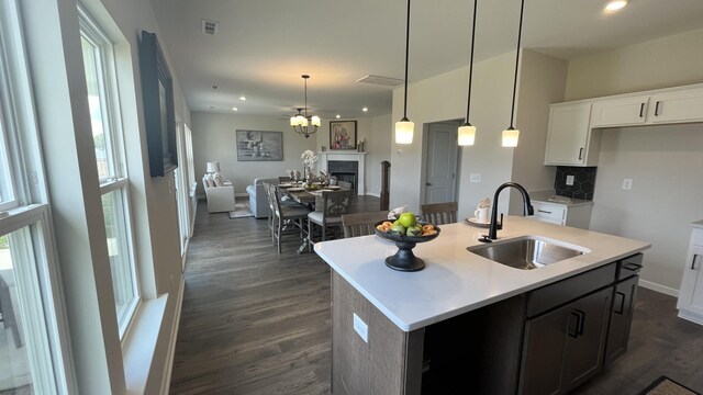 kitchen featuring dark hardwood / wood-style floors, tasteful backsplash, hanging light fixtures, a kitchen island with sink, and sink