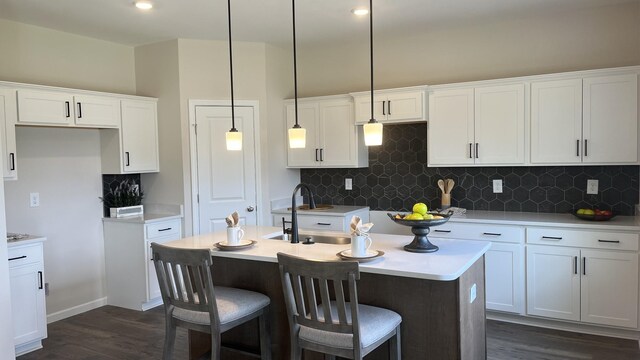 kitchen featuring backsplash, sink, dark wood-type flooring, a kitchen island with sink, and white cabinetry