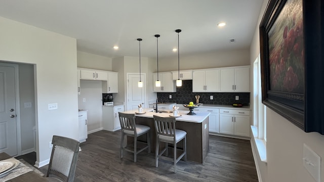 kitchen with dark hardwood / wood-style flooring, tasteful backsplash, hanging light fixtures, an island with sink, and white cabinetry