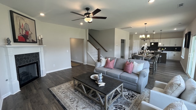 living room featuring a tiled fireplace, ceiling fan with notable chandelier, and dark hardwood / wood-style floors