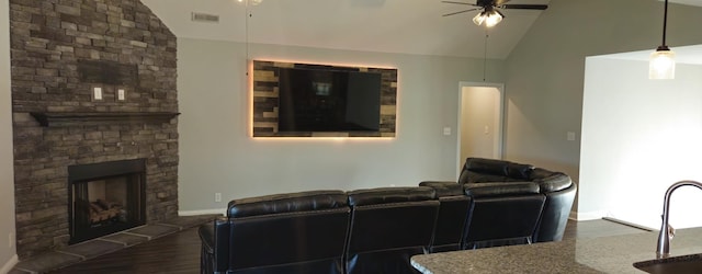 living area with visible vents, vaulted ceiling, a ceiling fan, and a stone fireplace