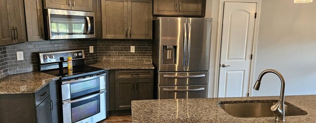 kitchen featuring decorative backsplash, hardwood / wood-style floors, appliances with stainless steel finishes, sink, and stone counters