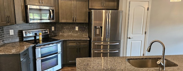 kitchen featuring decorative backsplash, light stone countertops, stainless steel appliances, dark brown cabinets, and a sink