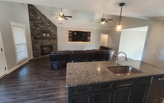 kitchen featuring stone counters, open floor plan, a kitchen island with sink, a sink, and a stone fireplace