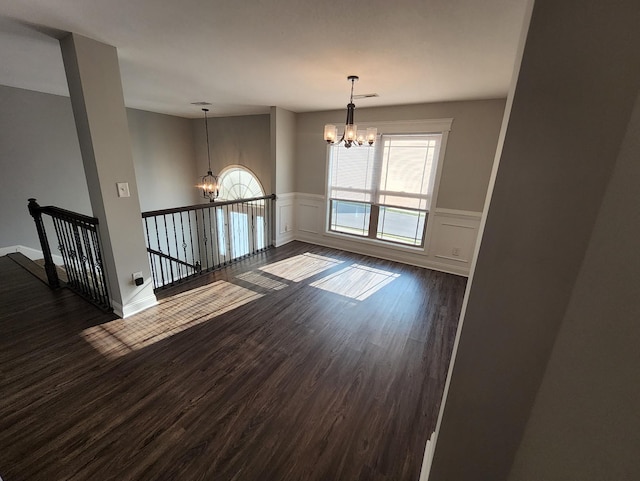 empty room with a chandelier, a wealth of natural light, and dark wood-type flooring