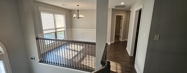 hallway with a wainscoted wall, dark wood finished floors, visible vents, a chandelier, and baseboards