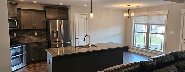 kitchen featuring dark hardwood / wood-style flooring, tasteful backsplash, appliances with stainless steel finishes, sink, and a center island with sink