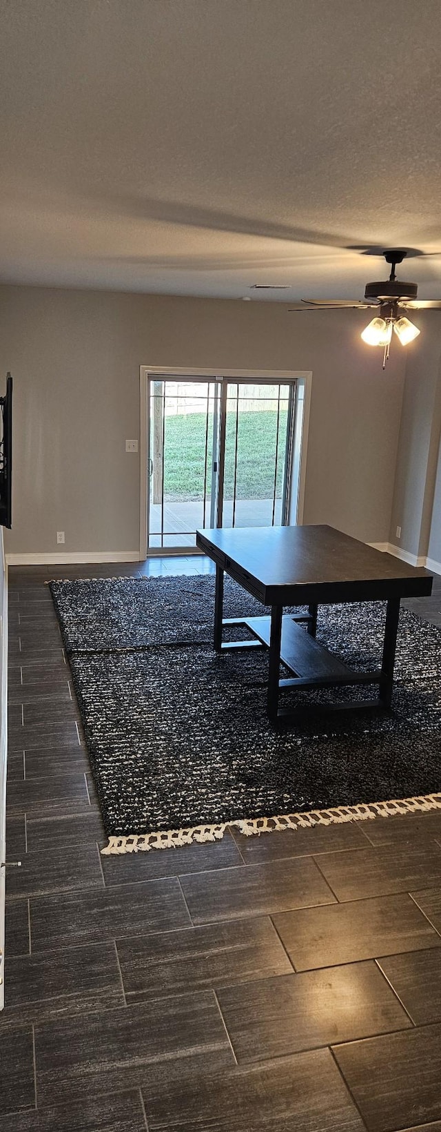 unfurnished dining area with a textured ceiling, dark wood-type flooring, a ceiling fan, and baseboards