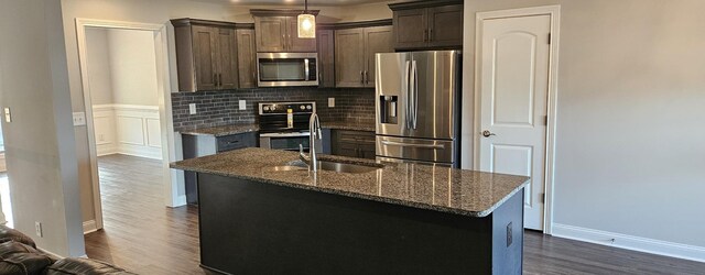 kitchen featuring backsplash, stainless steel appliances, a center island with sink, and dark hardwood / wood-style flooring