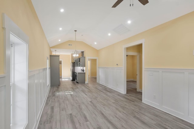 unfurnished living room featuring ceiling fan, a wainscoted wall, visible vents, vaulted ceiling, and light wood finished floors