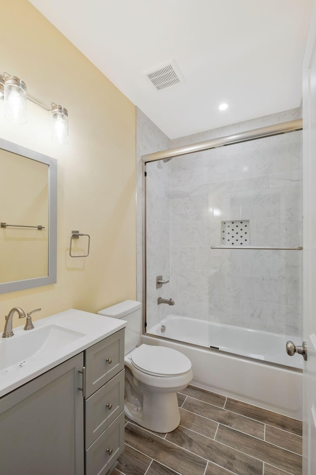 bathroom featuring bath / shower combo with glass door, visible vents, toilet, wood tiled floor, and vanity