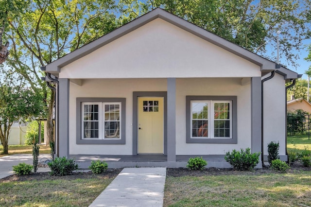 bungalow featuring a porch, a front yard, and stucco siding