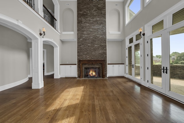 unfurnished living room featuring a fireplace, french doors, a towering ceiling, and dark wood-type flooring