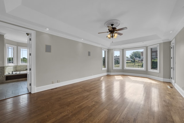 unfurnished living room featuring baseboards, dark wood finished floors, ceiling fan, a tray ceiling, and crown molding