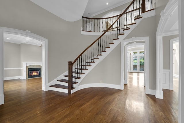 stairs with a glass covered fireplace, a towering ceiling, baseboards, and wood finished floors