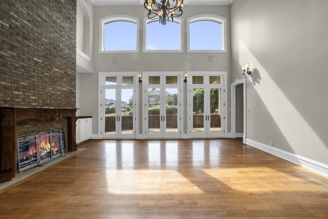 unfurnished living room featuring french doors, a fireplace, wood finished floors, and an inviting chandelier