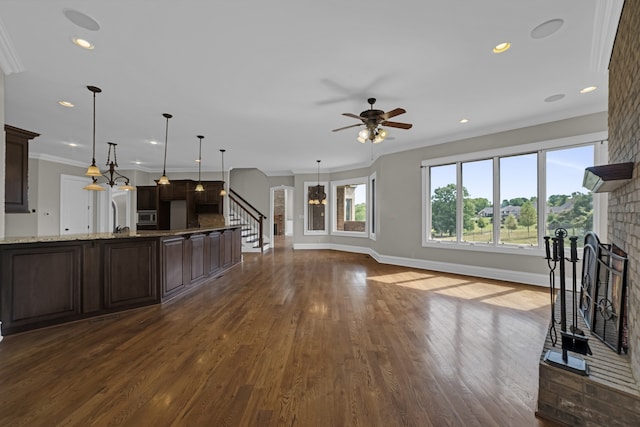 kitchen with crown molding, dark hardwood / wood-style flooring, a brick fireplace, ceiling fan, and light stone countertops