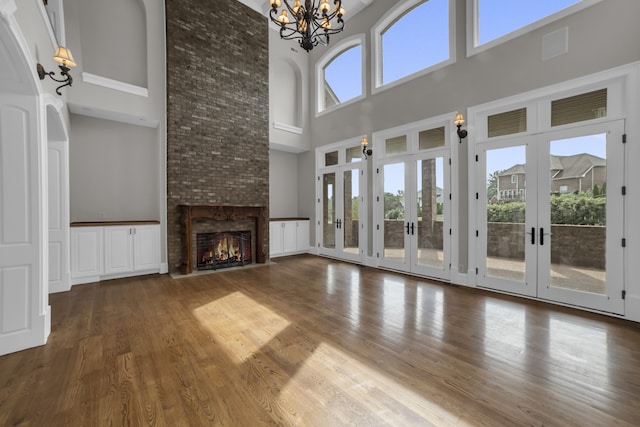 unfurnished living room with an inviting chandelier, a fireplace, french doors, hardwood / wood-style flooring, and a high ceiling