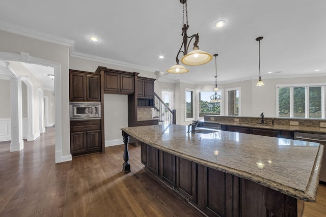 kitchen with appliances with stainless steel finishes, light stone countertops, a large island with sink, sink, and dark hardwood / wood-style floors