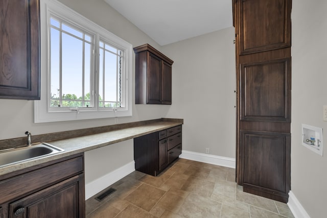 kitchen featuring a sink, visible vents, baseboards, dark brown cabinets, and built in study area