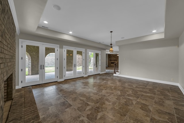 unfurnished living room with a tray ceiling, french doors, a fireplace, visible vents, and baseboards