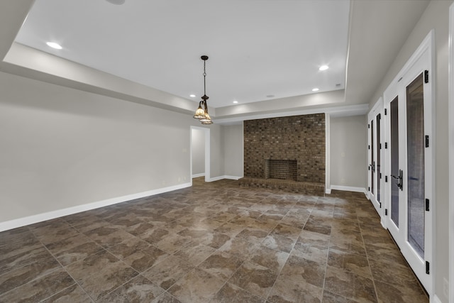 unfurnished living room featuring french doors, a tray ceiling, and a brick fireplace