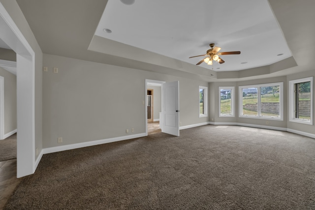 unfurnished living room featuring dark colored carpet, a raised ceiling, and baseboards