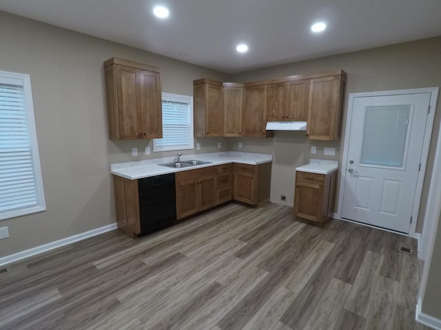 kitchen with under cabinet range hood, a sink, black dishwasher, light countertops, and brown cabinetry