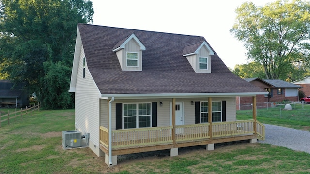 cape cod-style house with a porch, cooling unit, a shingled roof, fence, and a front lawn