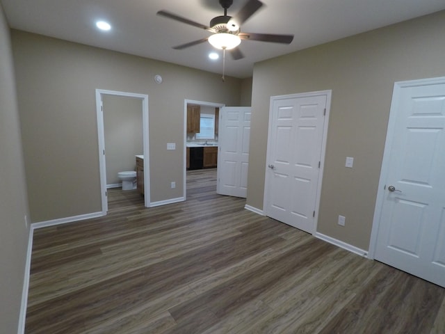 unfurnished bedroom with ensuite bathroom, a ceiling fan, two closets, baseboards, and dark wood finished floors