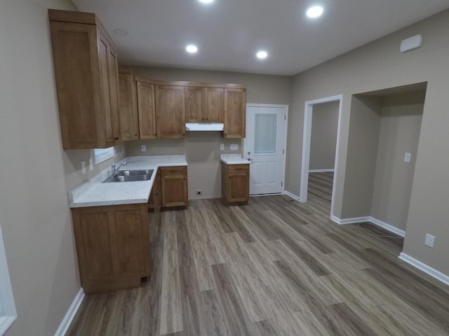 kitchen featuring light countertops, brown cabinetry, a sink, and under cabinet range hood