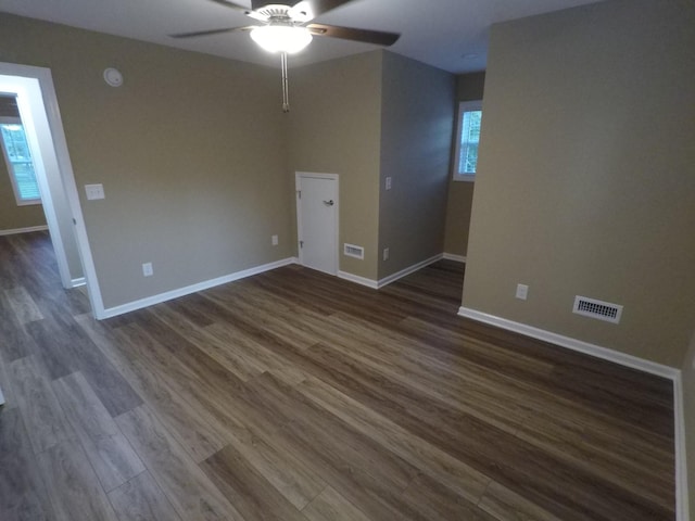 empty room with dark wood-style floors, baseboards, visible vents, and ceiling fan