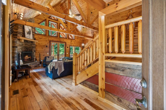 bedroom featuring wooden walls, light hardwood / wood-style floors, wooden ceiling, a fireplace, and lofted ceiling with beams