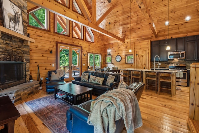 living room with high vaulted ceiling, light hardwood / wood-style floors, a stone fireplace, and beamed ceiling