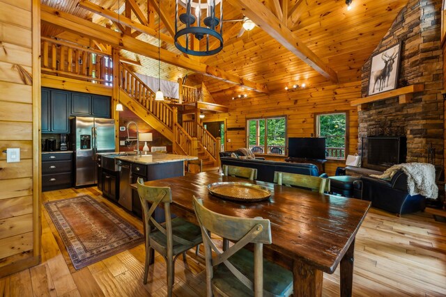 dining room with wood walls, beam ceiling, light hardwood / wood-style floors, a fireplace, and wooden ceiling