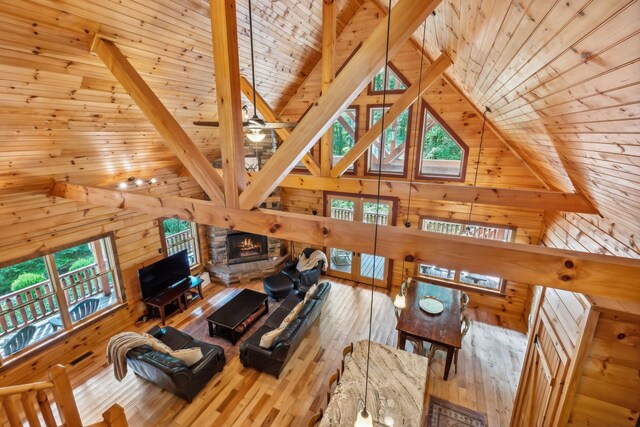 living room with wood walls, beam ceiling, hardwood / wood-style floors, wooden ceiling, and a stone fireplace